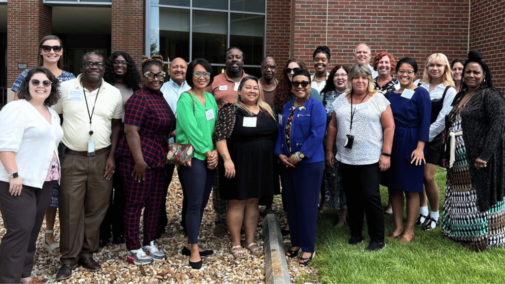 Diverse group of 21 public health professionals posting outside a building