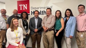 A group of nine people stands in front of a sign that reads TN Department of Health. They are smiling and posed for a group photo_1600x900